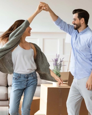 Ein junges Paar, welches in ihr Eigenheim einzieht und im Wohnzimmer tanzt.